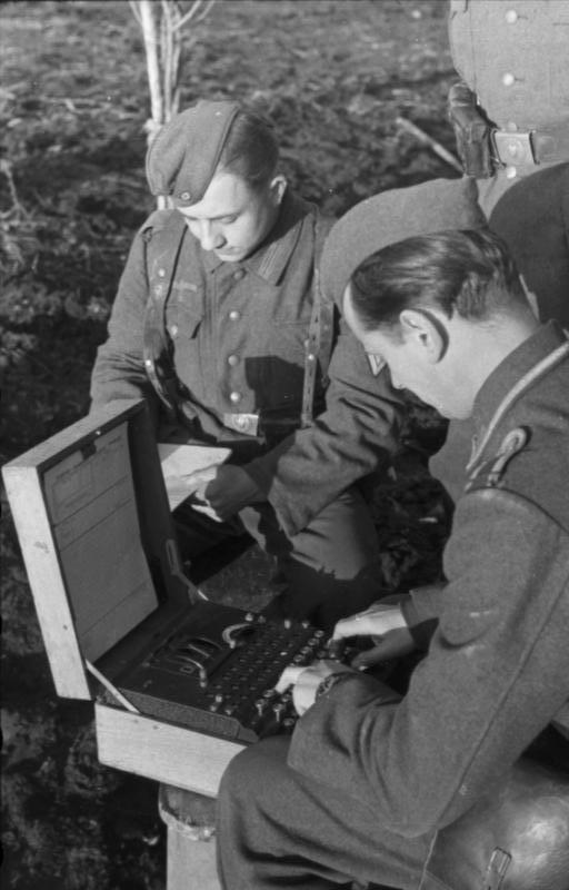Two soldiers work with an open Enigma machine outdoors, one typing while the other holds a message sheet.